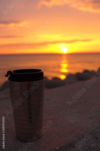 Close shot of a tumbler against background of Sunset over Yellow Sea. Golden sky with clouds.
