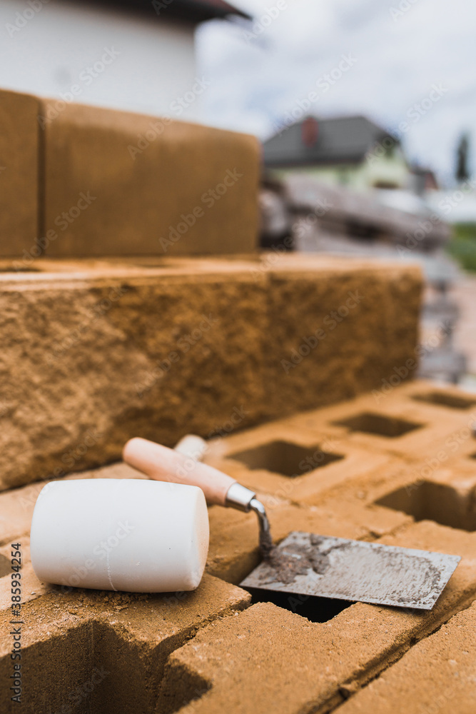 Mason tools in the workplace - a trowel and a mallet lie on a concrete block wall under construction