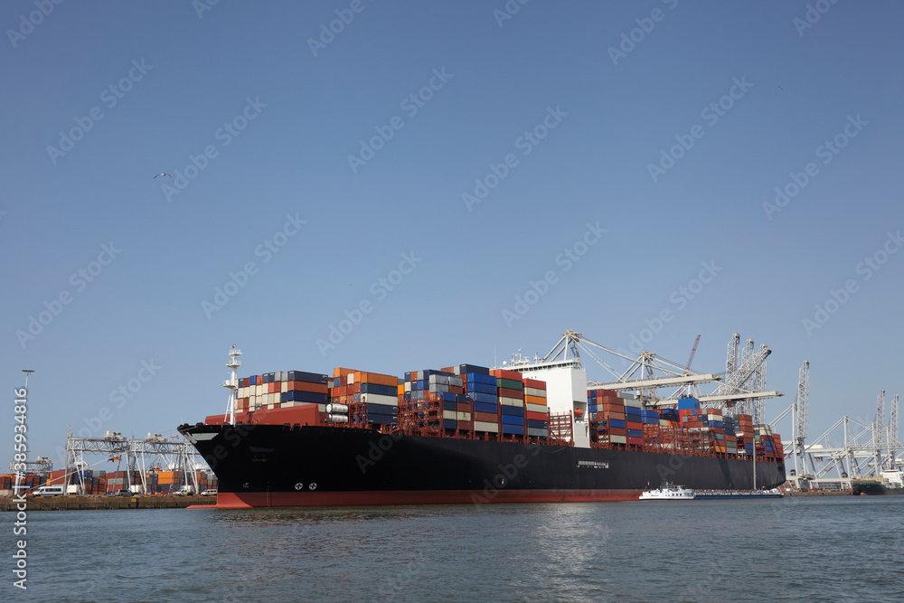 Rotterdam, The Netherlands. View of a large containership docked in the container terminal loading and unloading containers on land and river barge moored next to the containership