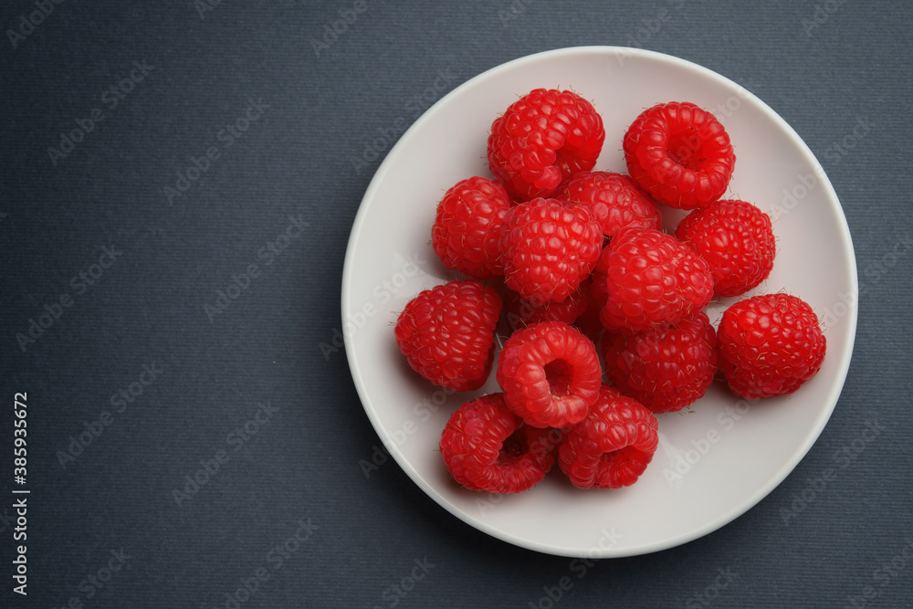 Raspberry berries on a white plate on a black background Raspberry berries on a white plate on a black background