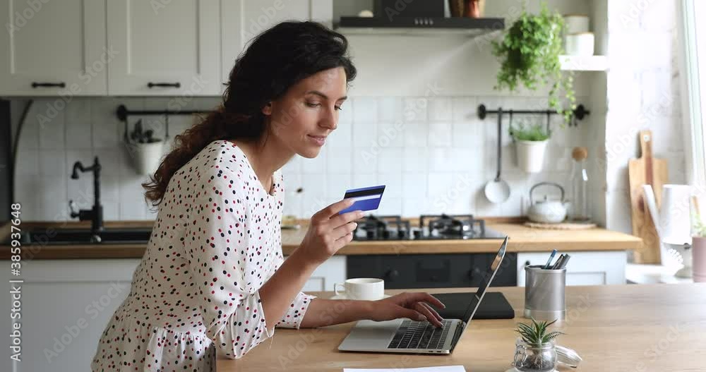 Woman standing in domestic kitchen using portable computer enter credit card numbers buying on internet, booking hotel. Housewife paying for food delivery order, secure easy electronic payment concept Woman standing in domestic kitchen using portable computer enter credit card numbers buying on internet, booking hotel. Housewife paying for food delivery order, secure easy electronic payment concept