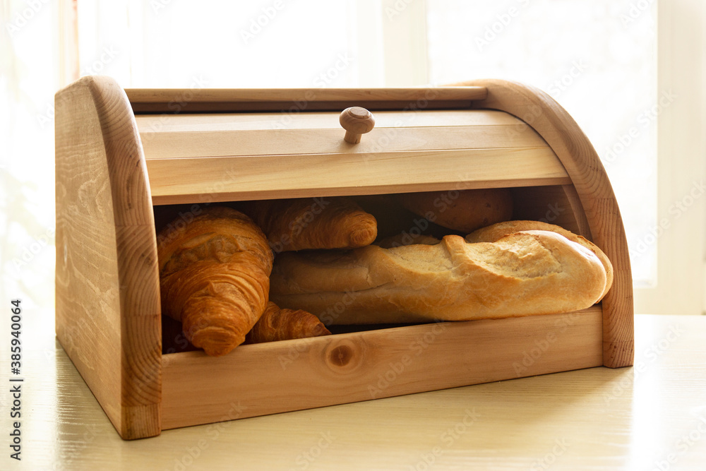 Wooden bread box full of different bakery on the bright sunlight background. Fresh baguette and croissants in the breadbox. - obrazy, fototapety, plakaty 