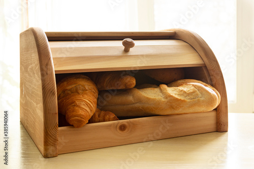 Wooden bread box full of different bakery on the bright sunlight background. Fresh baguette and croissants in the breadbox. photo