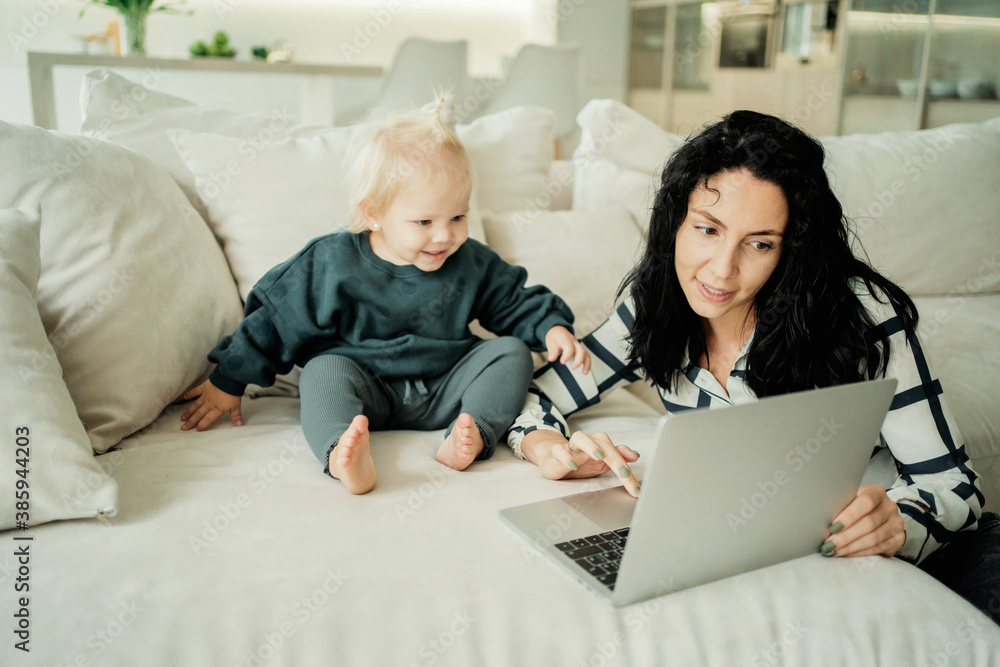 portrait of a young single mother brunette and blonde daughter children look at the gadget computer laptop gray, children's entertainment programs. Stylish, comfortable, modern clothing portrait of a young single mother brunette and blonde daughter children look at the gadget computer laptop gray, children's entertainment programs. Stylish, comfortable, modern clothing