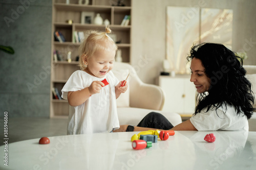 Billede på lærred little cute blonde girl of European appearance baby and nanny brunette play with children's toys in the living room