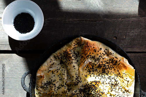 Nigella sativa also known as black cumin. Bread covered with black seeds in shadow with wood background. Burek photo
