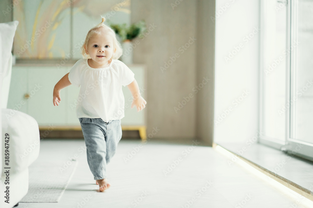 portrait of a girl child kids running around playing in the apartment, dressed in a white shirt and blue jeans. white apartment design, daylight in the window portrait of a girl child kids running around playing in the apartment, dressed in a white shirt and blue jeans. white apartment design, daylight in the window