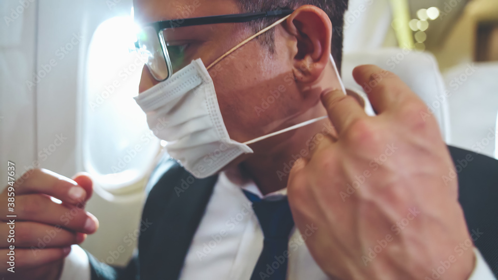Traveler wearing face mask while traveling on commercial airplane . Concept of coronavirus disease or COVID 19 pandemic outbreak effects on tourism and airline business . - obrazy, fototapety, plakaty 