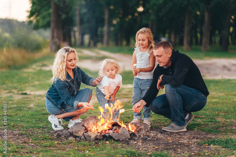 Mother, father and two children are sitting on a grass by the fire and having rest.
