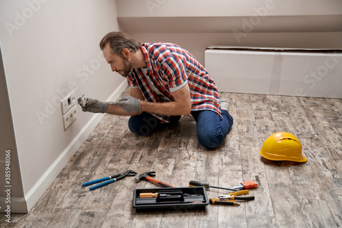 Foto Young caucasian electrician putting power socket into wall