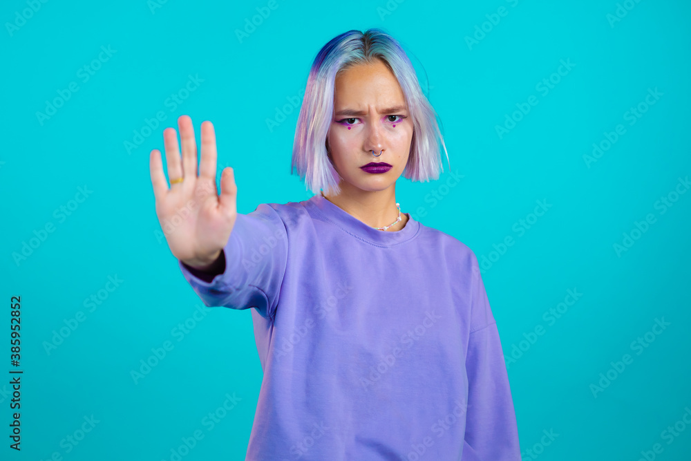 Pretty woman with violet hair disapproving with NO hand sign gesture. Denying, rejecting, disagree, portrait of beautiful hipster girl on blue background. Pretty woman with violet hair disapproving with NO hand sign gesture. Denying, rejecting, disagree, portrait of beautiful hipster girl on blue background.