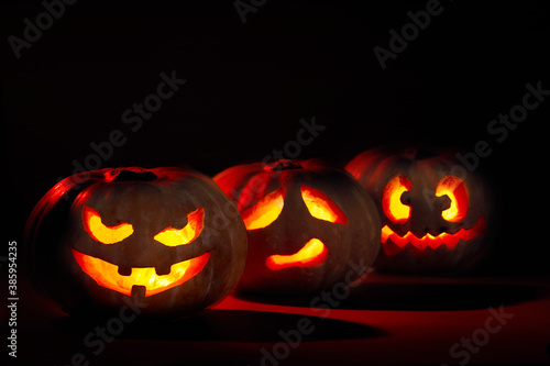 Three illuminated halloween pumpkins. With devilish, sad and crazy face on dark background with red light