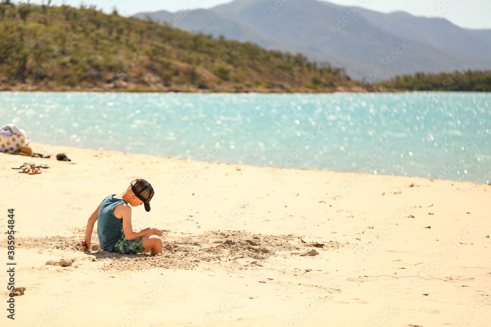 Boy wearing cap sitting on beach playing in sand Boy wearing cap sitting on beach playing in sand