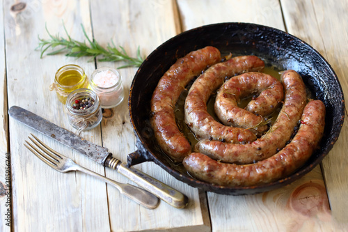 Selective focus. Fried homemade sausages in a frying pan on a wooden surface. Delicious Bavarian sausages.