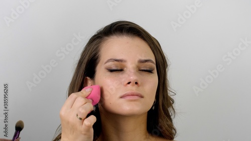 Professional make-up artist uses a sponge. Applying foundation with a pink cosmetics make up sponge. Attractive female face of a brunette well-groomed woman. 