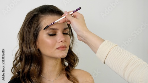 Attractive female face of a brunette well-groomed woman. Styling and lamination of eyebrows. Master combing patient’s eyebrows with a special brush. Eyebrow shaping with a cosmetic brush close-up.