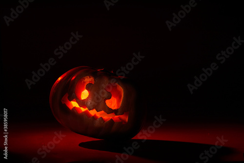 Illuminated halloween pumpkin with leaning crazy face on a dark background in red tones