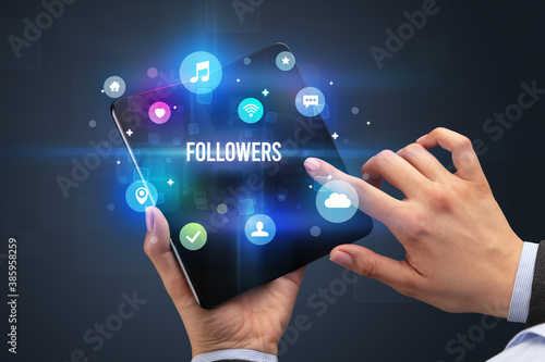 Businessman holding a foldable smartphone with FOLLOWERS inscription, social media concept