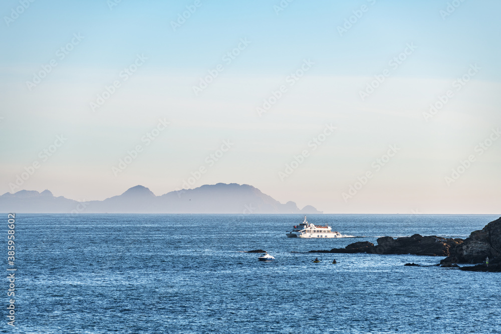 A lonely ferry cruises inside the Ria de Pontevedra in Galicia at dusk, with the Cies Islands in the background.