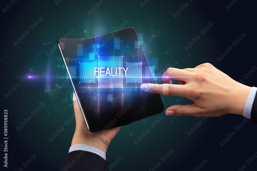 Businessman holding a foldable smartphone with REALITY inscription, new technology concept Businessman holding a foldable smartphone with REALITY inscription, new technology concept