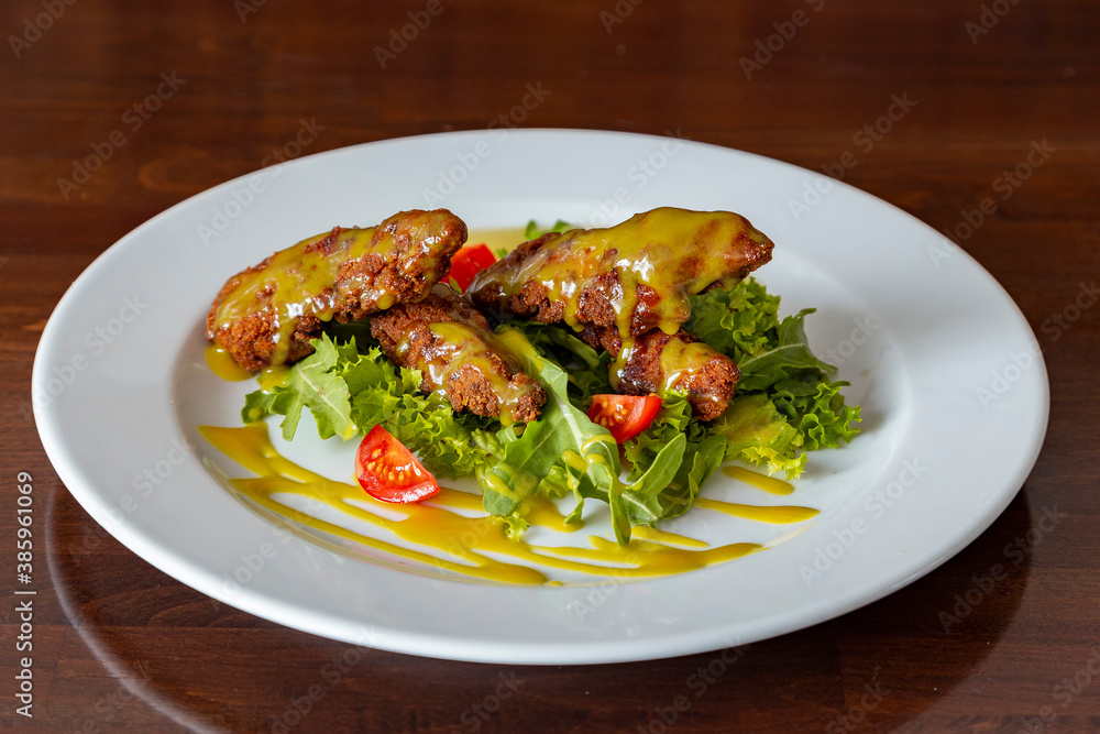 Chicken nuggets with tomatoes, herbs and sauce on a plate on a wooden background Chicken nuggets with tomatoes, herbs and sauce on a plate on a wooden background