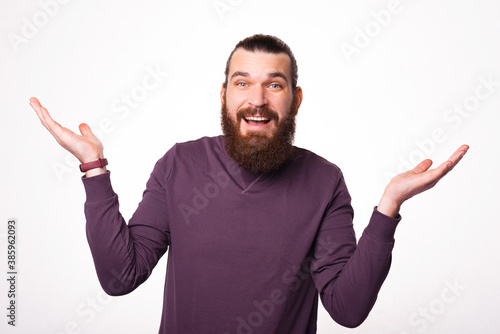 A bearded man is showing dont know gesture with a surprised face near a white wall