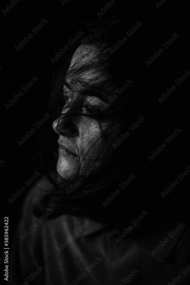 Moody black and white portrait of young caucasian woman, no makeup, natural look, dark background, looking away and thinking. Sad look. Tired and exhausted woman concept.