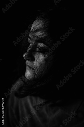 Moody black and white portrait of young caucasian woman, no makeup, natural look, dark background, looking away and thinking. Sad look. Tired and exhausted woman concept.