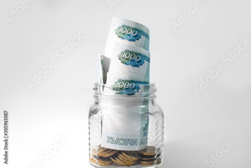 Banknotes and coins in a piggy bank close-up. A thousand rubles in a glass bottle, isolate on a white background. The concept of saving finances, economic crisis, falling income