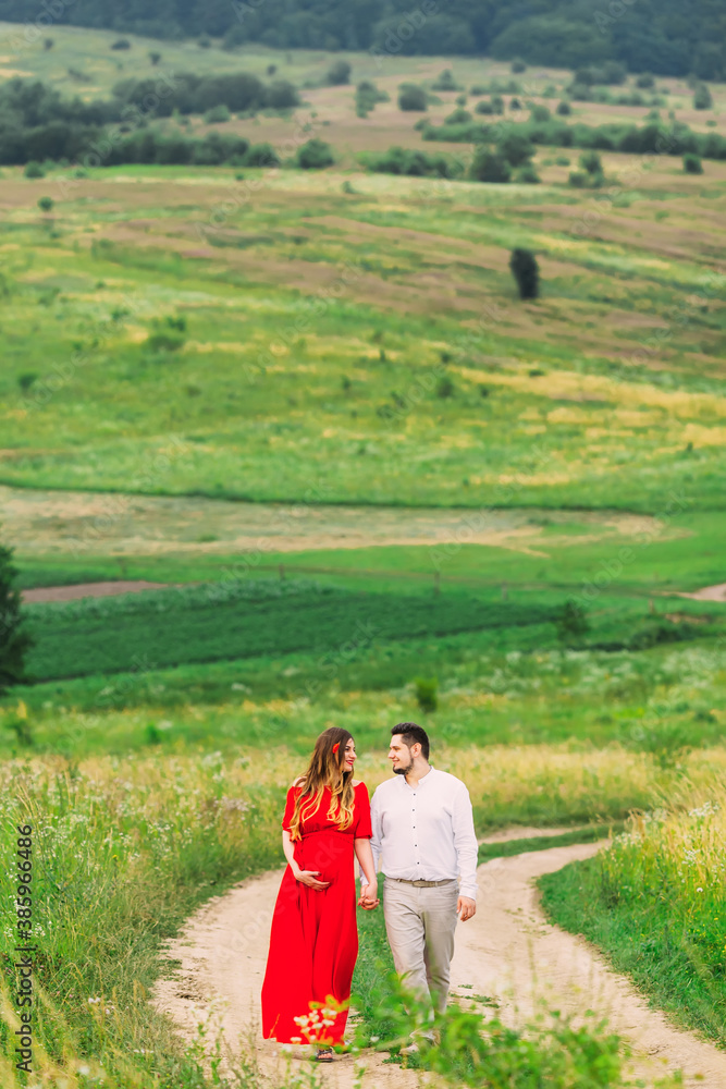 pregnant woman in red dress. future parents hold hands and walk pregnant woman in red dress. future parents hold hands and walk