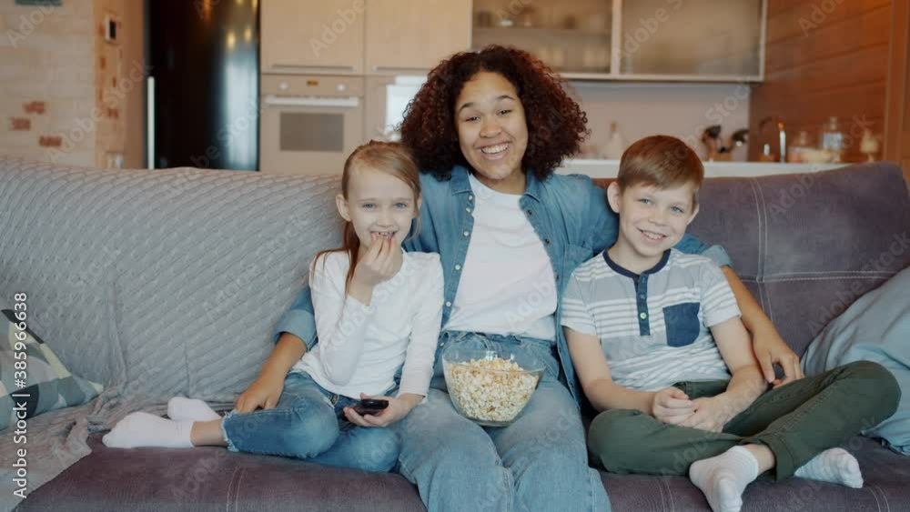 Portrait of happy young people nanny and kids watching TV and laughing looking at camera at home. Entertainment and modern technology concept. Portrait of happy young people nanny and kids watching TV and laughing looking at camera at home. Entertainment and modern technology concept.