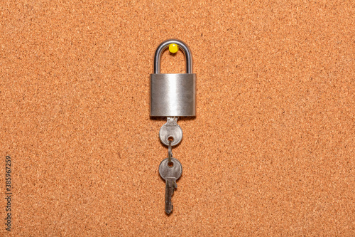 Closed padlock with keys hanging from it on an empty corkwood notice board in business office. Safety and security reminder, business closure, business for sale concepts.