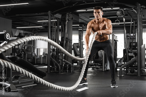 Muscular man working out with heavy ropes in gym. Strong male naked torso abs