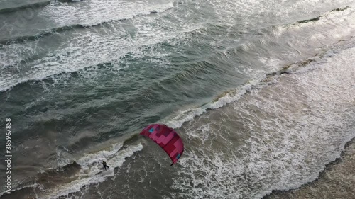 Riding big waves on kitesurfing in summer. 4K Drone view of the ocean and people engaged in extreme sports, kite surfing. Beautiful clear water Aerial view people kiteboarding ride.