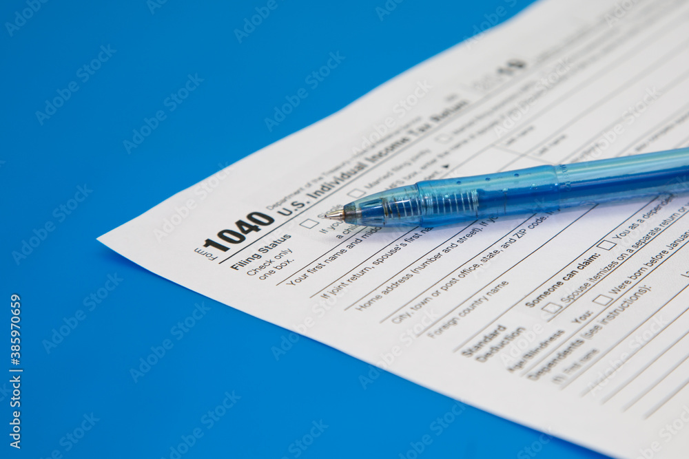 Obraz premium Tax return close-up on a blue background. Blue pen on tax form 1040. Selective focus