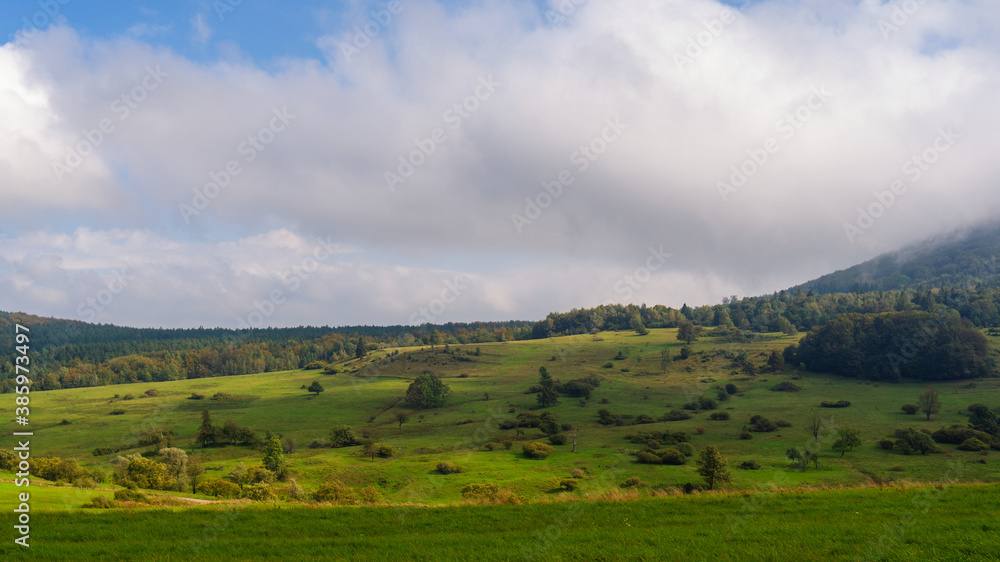 Landscape of Beskid Niski mountains. Regietow Wyzny in Lesser Poland. Grassy land and forested mountain hill. White cloud on sky.