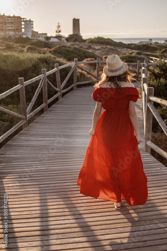 a female model walking down a wooden pathway away from the camera in a red dress  © josehidalgo87