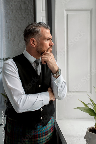 handsome mature courageous stylish scotsman (gay) in kilt by the window. Style, fashion, lifestyle, culture, ethnic concept. photo