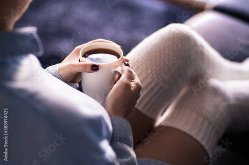 Cup of morning tea in winter. Woman with hot drink and warm cozy long socks on comfy home couch. Sick person with flu or fever. Comfortable relaxing on weekend. Healthy fashion lifestyle concept.