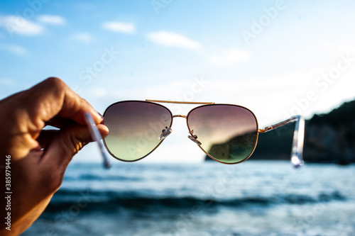 Sunglasses in the hands of a man on a background of the sea in sunny weather
