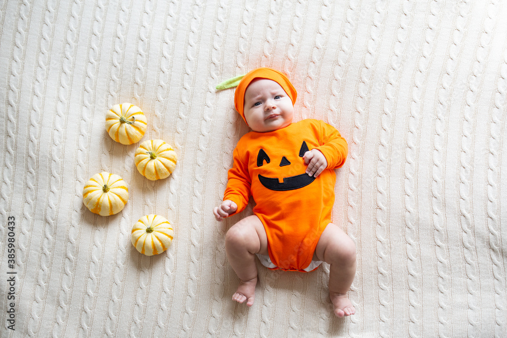 Fototapeta premium High Angle View Of Baby In Pumpkin Costume. Happy Kid two months old in orange Halloween costume on bed