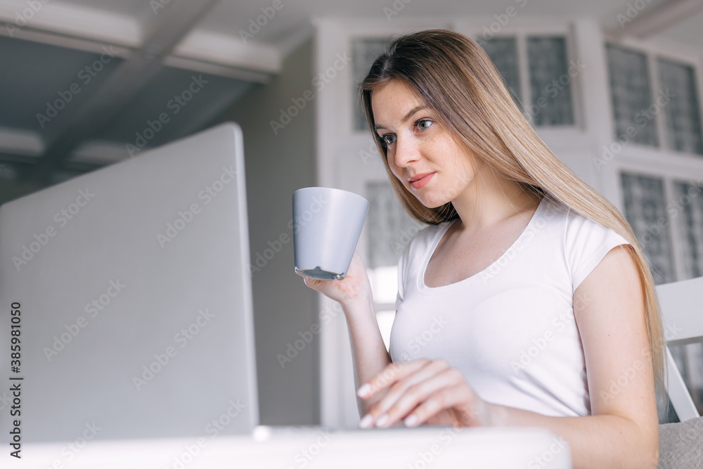 Serious woman drink coffee, using computer in kitchen at home. w Serious woman drink coffee, using computer in kitchen at home. w