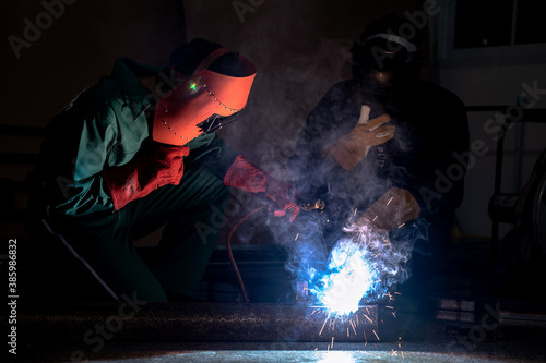Workers weld metal with a arc welding machine at industrial facility.