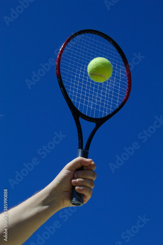 Raquete de tênis com bola amarela e fundo do céu azul