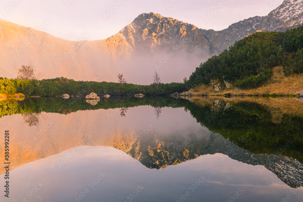 High mountains are reflected in a mountain clear lake with inverse autumn clouds