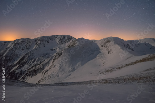 Winter landscape in a mountainous environment in the dark under a night sky full of stars at moonlight