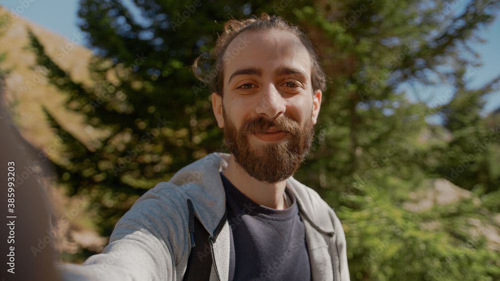 Smile face hippie climber with his backpack behind him, with his handheld camera or phone, salutes the audience or the person he is talking, vlogger or video chat in nature concept Smile face hippie climber with his backpack behind him, with his handheld camera or phone, salutes the audience or the person he is talking, vlogger or video chat in nature concept