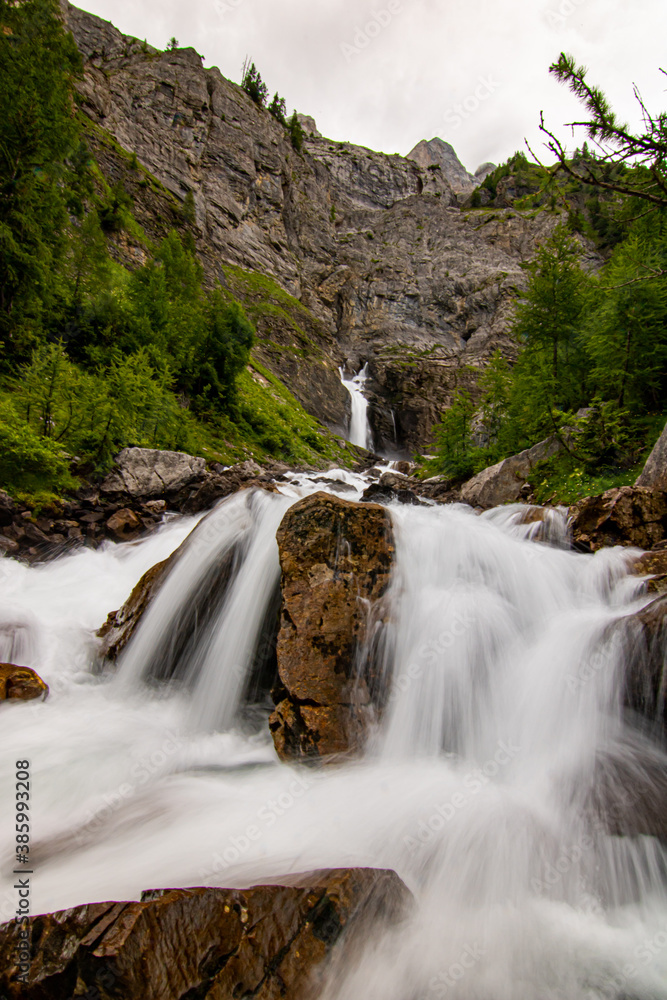 Obraz premium Small waterfalls streaming in green forest in long exposure. water in motion - swiss Alps
