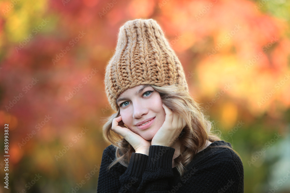 Portrait of a woman in a knitted hat against a background of autumn trees. Beautiful smiling girl. Handmade hats. Warm clothes. Autumn season. Portrait of a woman in a knitted hat against a background of autumn trees. Beautiful smiling girl. Handmade hats. Warm clothes. Autumn season.