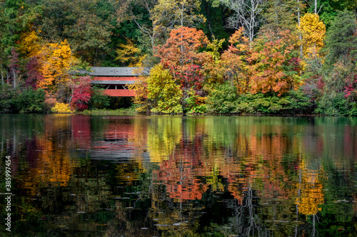 With a beautiful reflection on Lake Loretta in Alley Park, Lancaster, Ohio, the red George Hutchins Covered Bridge, surrounded by colorful autumn leaves, was constructed in 1865 at another location Fototapet
